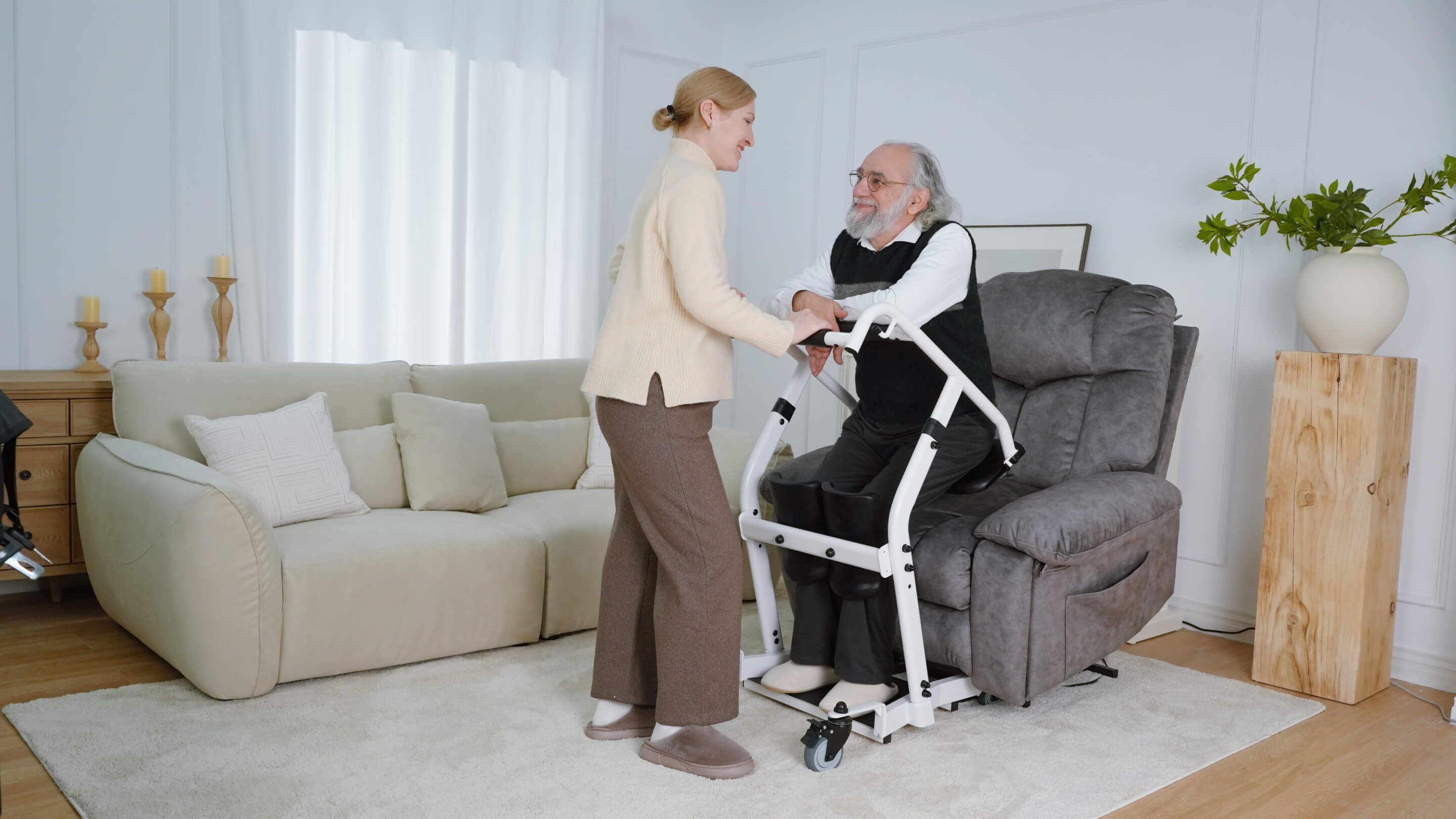 A caregiver assisting an older man with a standing transfer aid at home.
